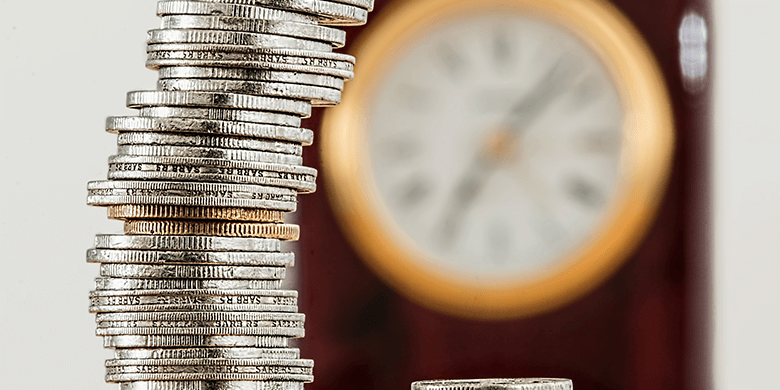 A stack of coins sitting in front of a blurred out clock.